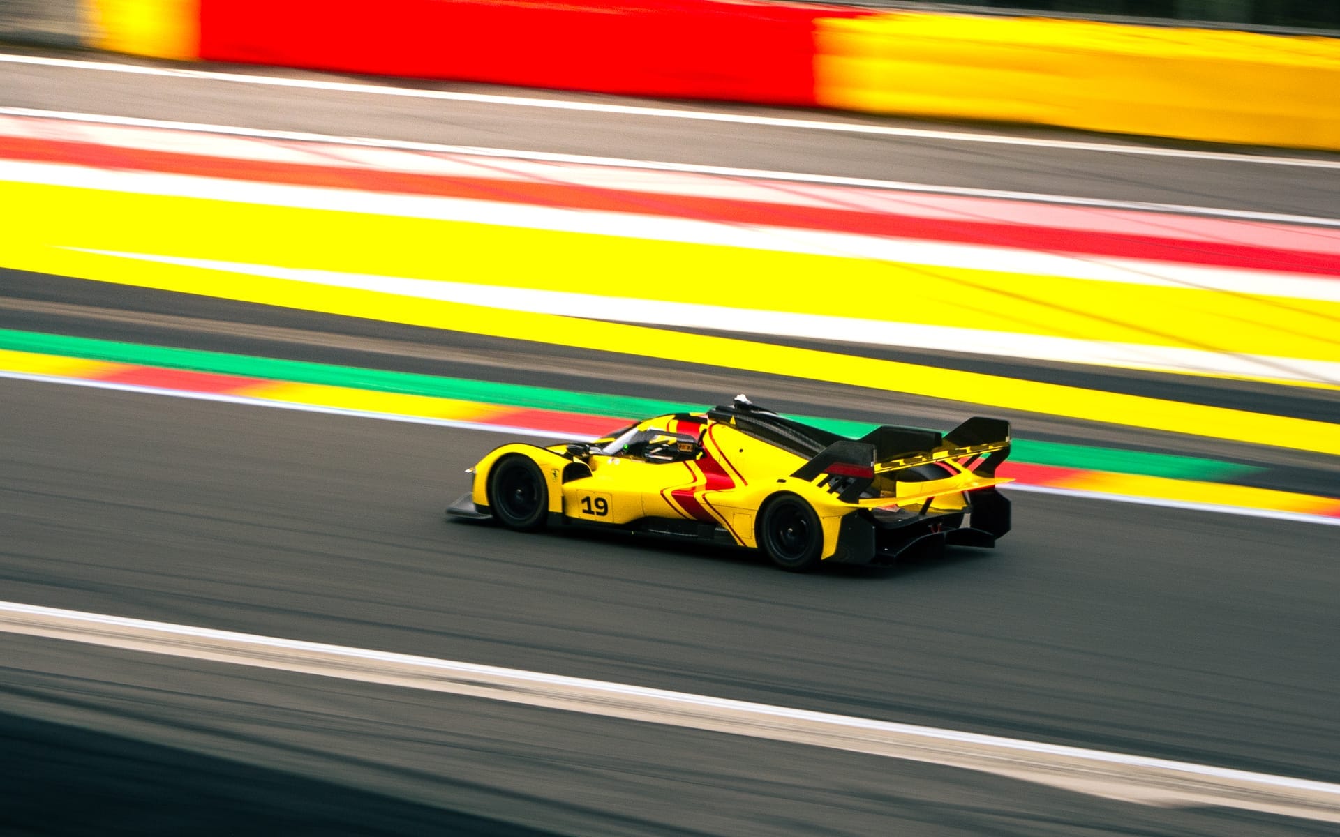Gele raceauto in volle vaart langs de kleurrijke kerbs van het circuit van Spa-Francorchamps